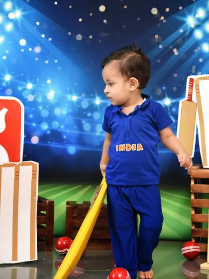 Taking his stance, this little batsman is ready for action. The dynamic stadium backdrop adds energy and excitement to the cricket-themed shoot.
