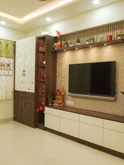 A comprehensive view of a living room entertainment wall, combining a TV unit, a CNC-cut pooja cabinet, and a tall glass display case. This multifunctional design is perfect for modern homes.