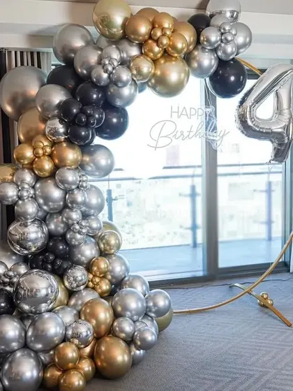 A 40th birthday celebration with a stylish balloon arch in black, gold, and silver against a large window.