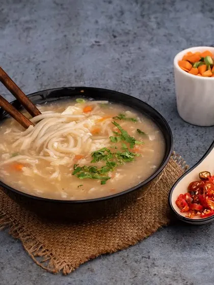 A warm and comforting bowl of chicken noodle soup. The styling focuses on the delicate noodles and fresh ingredients, creating a simple yet elegant shot for our client's menu.