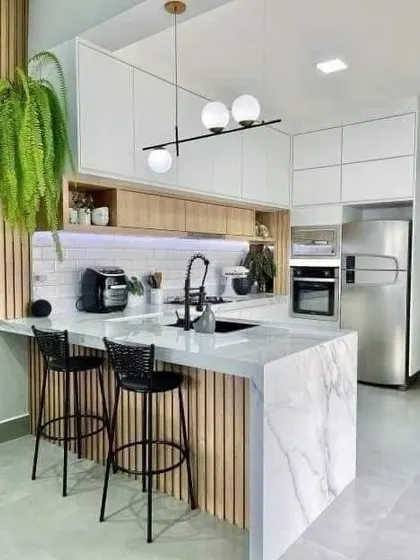 This kitchen design incorporates a breakfast bar with a waterfall marble countertop. The combination of white marble, light wood, and black accents creates a chic and modern Scandinavian look.