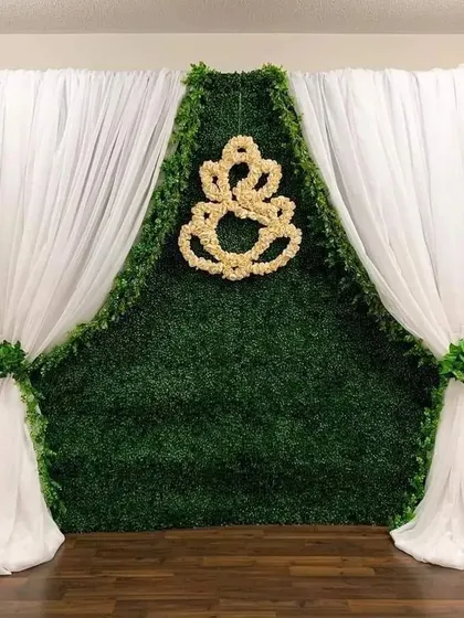 A simple and elegant backdrop using a green hedge wall and a floral Ganesha motif. The clean white drapes frame the setup, making it perfect for a small ceremony or home event.