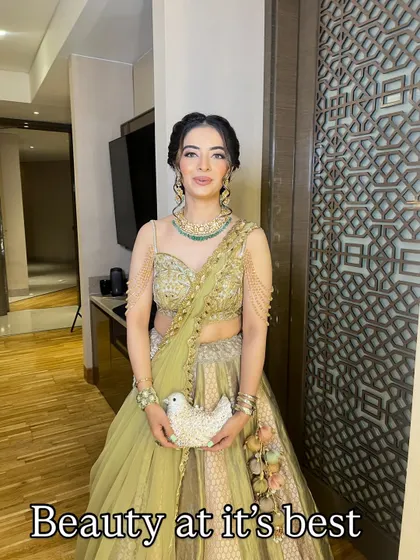 A full-length photo of the same bride, holding a unique bird-shaped clutch. Her makeup is fresh and radiant, perfect for an engagement or sangeet.