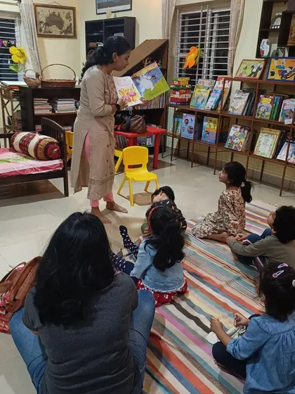 The storyteller stands to read, allowing all the children in the group to see the illustrations clearly.