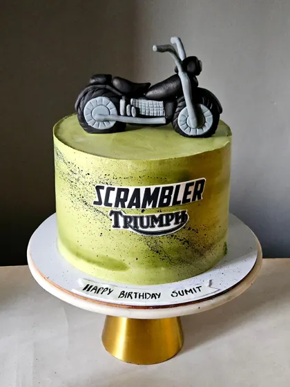 A cool and stylish cake for a motorcycle enthusiast. This design features a lime green airbrushed cake with a "Scrambler Triumph" logo and a detailed, hand-sculpted edible motorcycle on top.