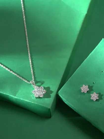 A delicate and modern silver-toned necklace set. The design features a simple floral pendant made of sparkling stones, with matching minimalist stud earrings.