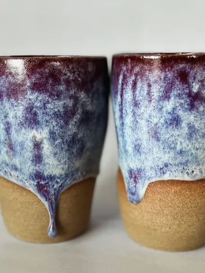 A close-up of two drip grip tumblers. You can see the rich texture and color variations in the glaze.