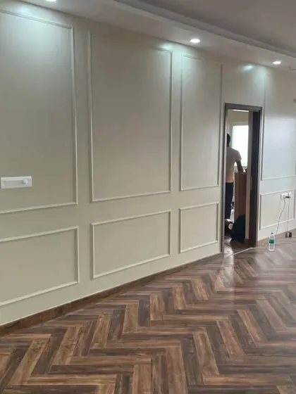 A living room during the finishing stages, with newly installed herringbone wooden flooring and classic wall molding. This highlights our expertise in flooring and wall treatments.