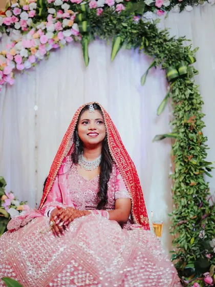 A beautiful solo portrait of the bride seated before a floral arch. She is wearing her red chunari, looking radiant and serene during her engagement ceremony.