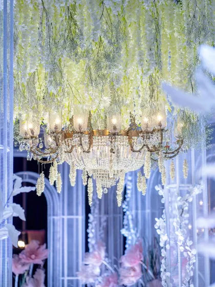 A classic crystal chandelier hangs amidst a canopy of white wisteria. This detail shot shows how I layer light and floral elements to create a sense of depth and opulence in my ceiling designs.