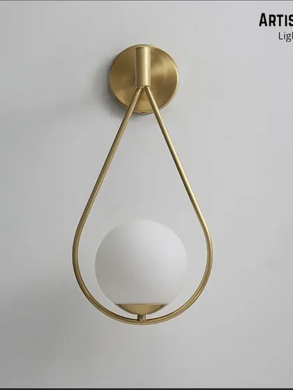 Inspired by a falling drop of rain, this wall light features a frosted white globe delicately held within a teardrop-shaped brass frame. It is a poetic and graceful addition to any contemporary space.