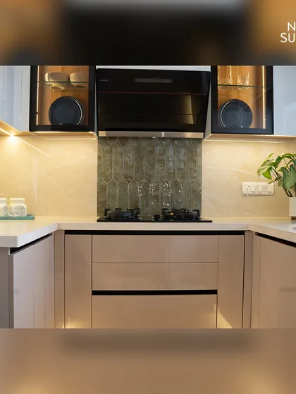 A close-up of the cooking area, featuring a sleek black chimney and an elegant backsplash. The combination of taupe cabinets, a white countertop, and glass-front upper cabinets creates a light and airy feel.