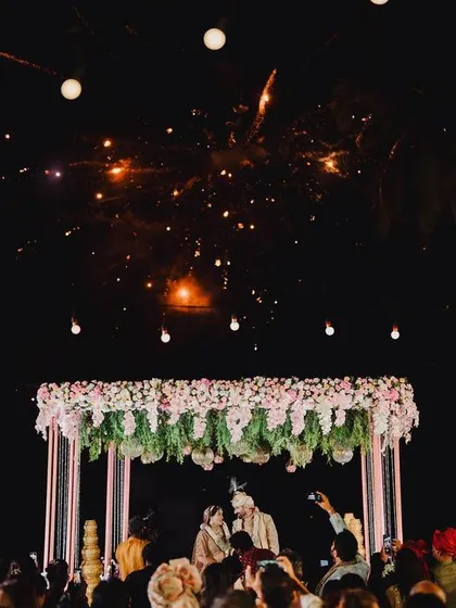 A wide shot of the Varmala ceremony under the night sky, with fireworks adding to the celebration.