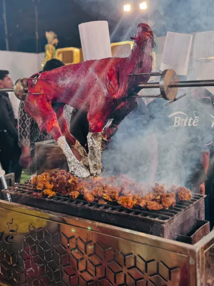 A close-up of the whole roasted mutton, showing the rich color and texture as it cooks over hot coals.