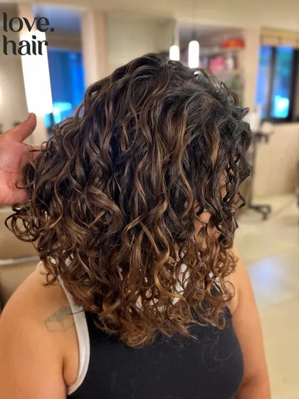 Lush, defined curls with a hint of color. We gave this client a beautiful brunette balayage that enhances her natural texture, all while following the Curly Girl Method.