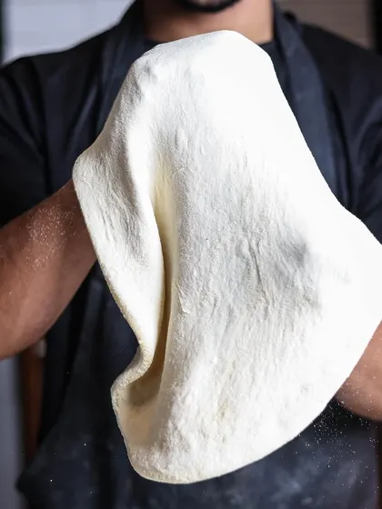 A chef skillfully stretches the pizza dough, a crucial step in creating the perfect thin base and puffy crust. It's an art form in itself.