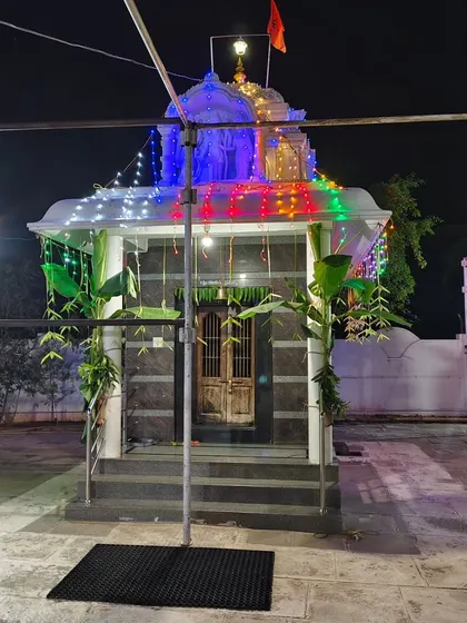 A small temple decorated for a night event with colorful lights, banana plantains, and simple leaf hangings.