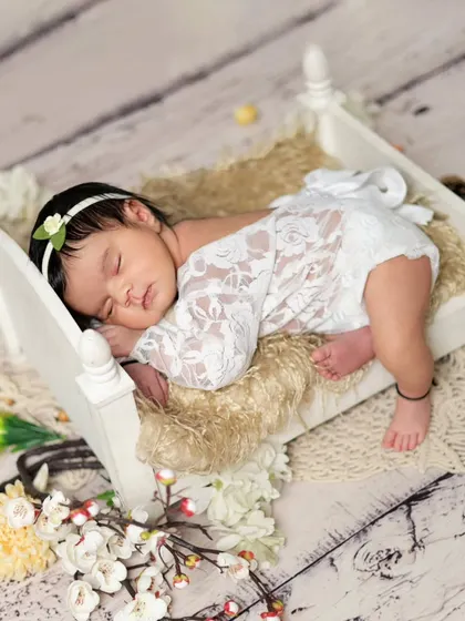 A sweet baby girl sleeping peacefully on a tiny wooden bed. We use delicate lace outfits and props to create timeless and classic newborn portraits.