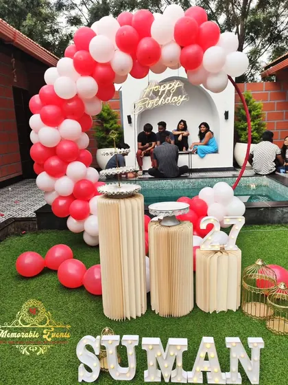 An outdoor poolside birthday decoration with a red and white balloon arch, perfect for a daytime celebration.