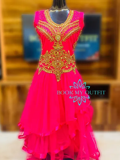 For a bold and vibrant pre-wedding look, consider this bright pink gown. It features intricate gold embroidery on the bodice and a layered, high-low skirt that adds texture and flair to your photos.