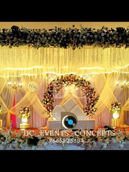 This stage backdrop uses warm lighting and shimmering fringe curtains to create a glamorous effect. The dense floral arrangements on top and sides add a touch of softness and romance to the overall design.