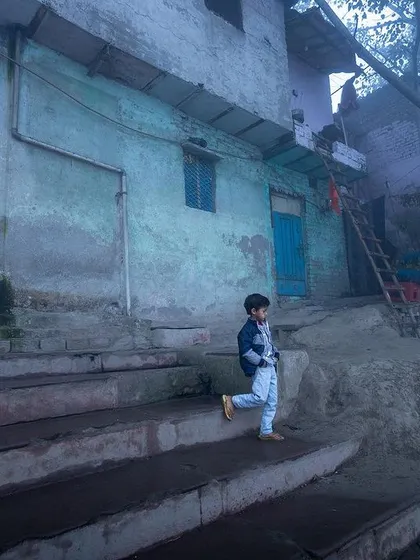 A young boy descends the steps of the ghat on a foggy morning, a slice of daily life captured in the ethereal mist.