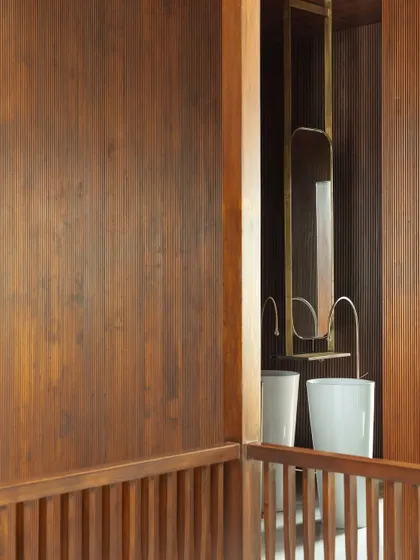 This view shows the careful detailing of a washroom, with rich wood paneling and custom brass fixtures reflected in a mirror, creating layers of texture and warmth.