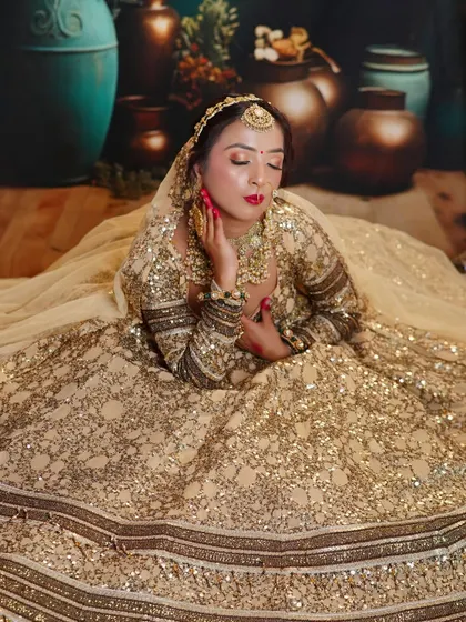 A close-up of a glamorous bridal look in a sequined gold lehenga. The focus is on the flawless makeup, bold red lip, and the intricate details of the heavy bridal jewellery.