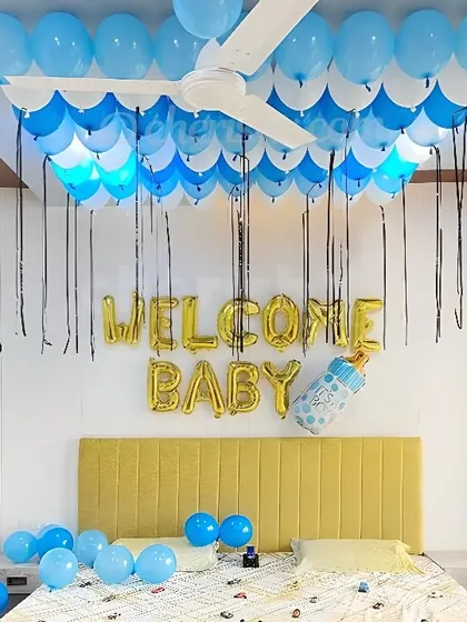 A simple 'Welcome Baby' bedroom decoration. The ceiling is covered with blue and white balloons, with gold foil letters above the headboard.