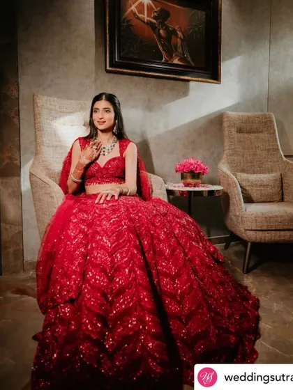 A full-length portrait of the bride, showcasing her stunning red engagement lehenga. The makeup look is polished and radiant.