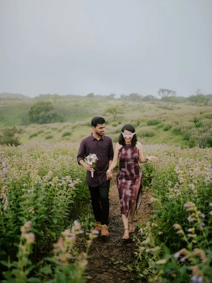 A couple walks hand-in-hand through a misty field of flowers during their pre-wedding shoot.