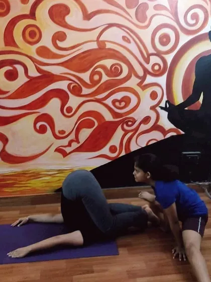 A mother gets support from her daughter while practicing Karnapidasana (Ear Pressure Pose). This beautiful moment shows how yoga can be a shared journey of encouragement across generations.