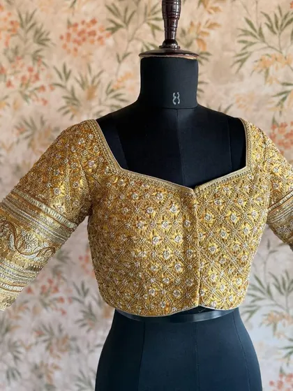 The front view of a heavily embroidered gold blouse. The square neckline and detailed sleeves make it a regal choice for any bride.