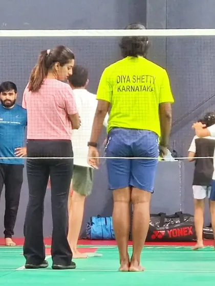 Discussing technique and form with a young athlete and her coach on the badminton court.