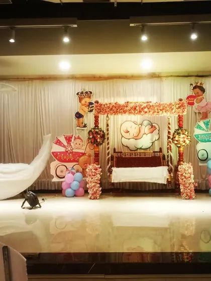 A traditional 'rukhwat' or 'otibharan' setup for a baby shower. The stage includes a decorated swing and a lighted moon prop, ready for the ceremony.