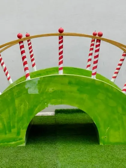 This whimsical wooden bridge prop, painted in bright green with candy-cane striped railings, is perfect for a Candyland, carnival, or elf-themed party.
