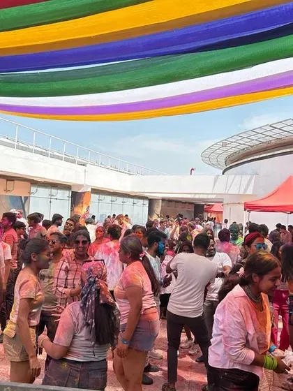 A wide shot of the rooftop Holi party. The colorful streamers and the packed crowd show the scale and success of the event.