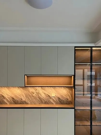 A stylish storage and display unit. The design uses a mix of closed cabinets, an open niche with a marble-finish backsplash, and a glass-door display case.
