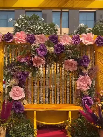 A seating area for a Haldi ceremony, framed in yellow and decorated with large paper flowers and marigold strings. This provides a beautiful and comfortable spot for the main rituals.