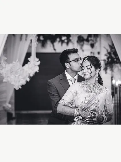 A tender black and white portrait of a groom kissing his bride's forehead at their reception.
