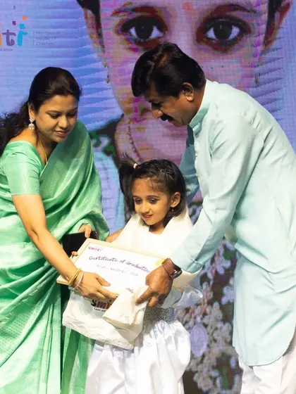 A girl receives her graduation certificate, surrounded by the applause of her teachers, family, and friends.