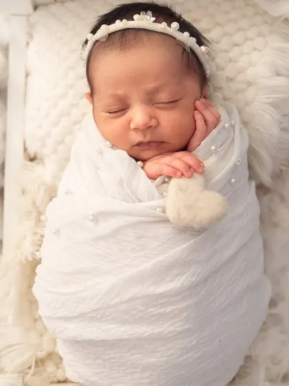 An overhead shot showing the baby swaddled in white, nestled in a bed of soft, fluffy clouds, creating a perfect little angel portrait.