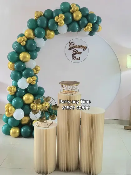 A green and gold balloon arch against a white circular backdrop for a "Growing Glow Bash".