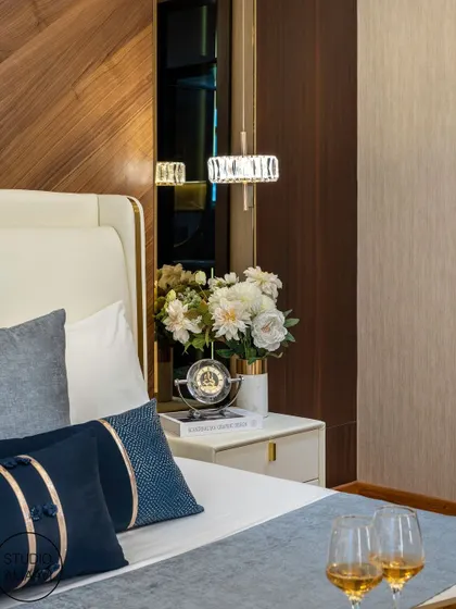 A detail shot of the bedside table, featuring a crystal lamp, fresh flowers, and a small clock. The rich wood paneling and deep blue pillows in the background highlight our meticulous approach to styling and creating a luxurious feel.