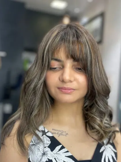 A trendy hairstyle featuring soft waves and stylish bangs. The highlights around the face brighten her complexion and complete the look.