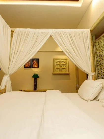 A low-angle view from the bed, emphasizing the crisp white linens and the intricate jali-style screen. This detail shot highlights the craftsmanship and unique architectural elements.