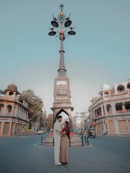 A stunning wide shot of a couple embracing in the middle of a historic Jaipur intersection, framed by the architecture and a vintage-style clock tower.