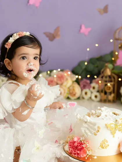 This shot captures the baby mid-snack, with a beautifully decorated butterfly cake in a lavender-themed setup.