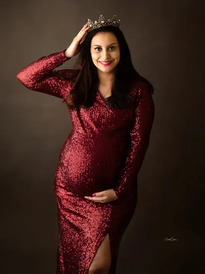 A portrait of pure confidence and joy. This mom-to-be adjusts her crown while wearing a sparkling red sequin gown, ready for her royal debut.