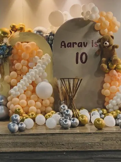 A soft and modern theme for a 10th birthday, using peach, silver, and gold balloons with a teddy bear accent.